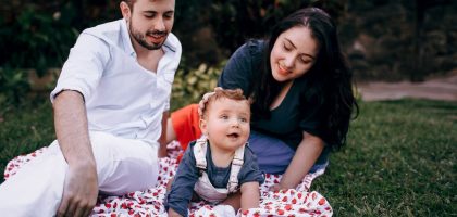 A joyful family enjoying a picnic outdoors during summer. Smiling parents with their baby on a blanket.