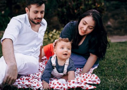 A joyful family enjoying a picnic outdoors during summer. Smiling parents with their baby on a blanket.