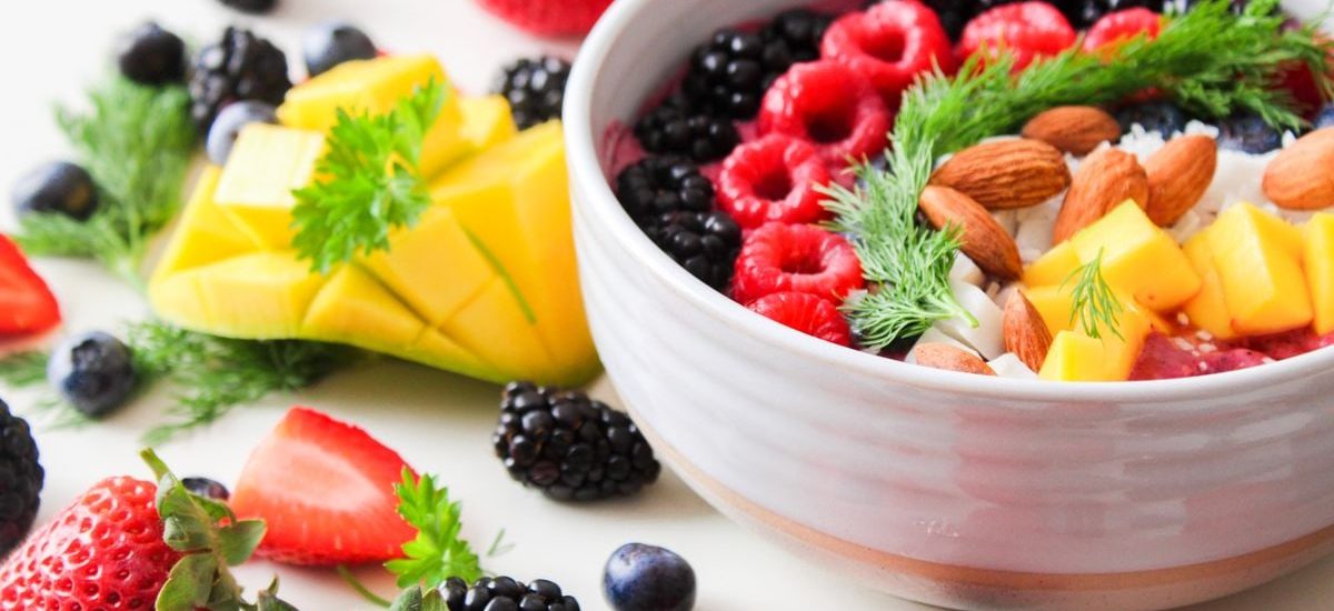 A vibrant bowl filled with fresh berries, mango, almonds, and herbs, perfect for a healthy snack or breakfast.