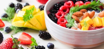 A vibrant bowl filled with fresh berries, mango, almonds, and herbs, perfect for a healthy snack or breakfast.