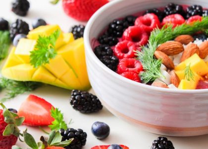 A vibrant bowl filled with fresh berries, mango, almonds, and herbs, perfect for a healthy snack or breakfast.